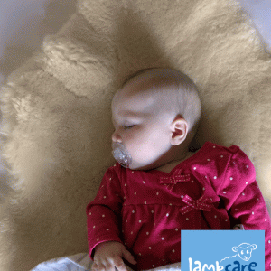 Baby girl with a hot pink top and pacifier asleep on a lambskin rug