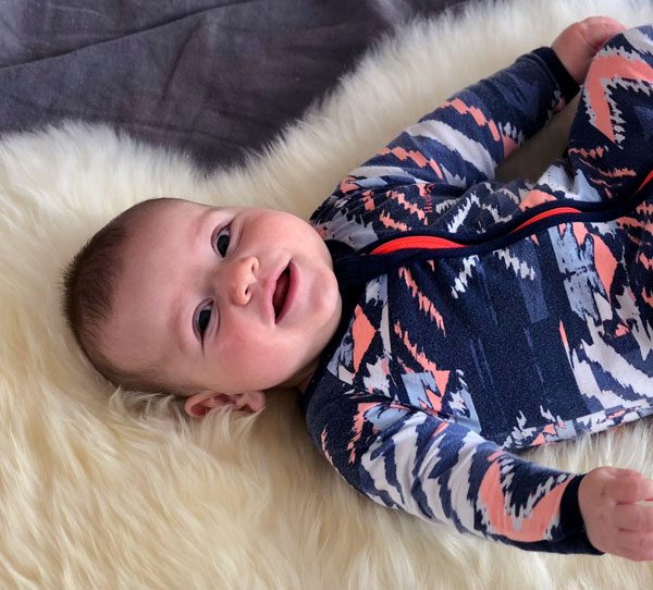 Smiling baby in romper suit on long wool ivory rug
