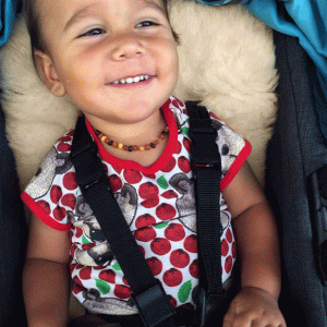 Smiling toddler sitting on a lambskin stroller liner in his stroller