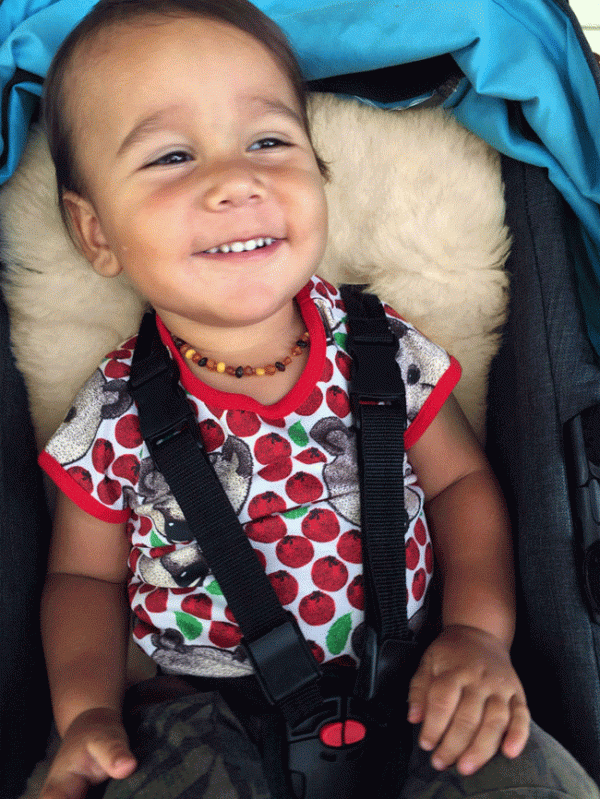 Smiling toddler sitting on a lambskin stroller liner in his stroller