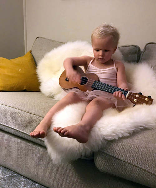 Young girl playing ukelele on long wool lambskin rug